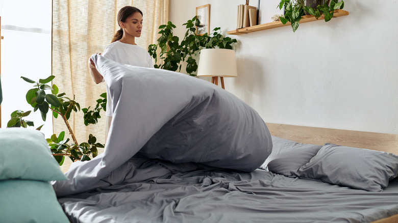 woman airing out duvet - The Biggest Secrets To Keeping Your Bedding Fresh & Clean