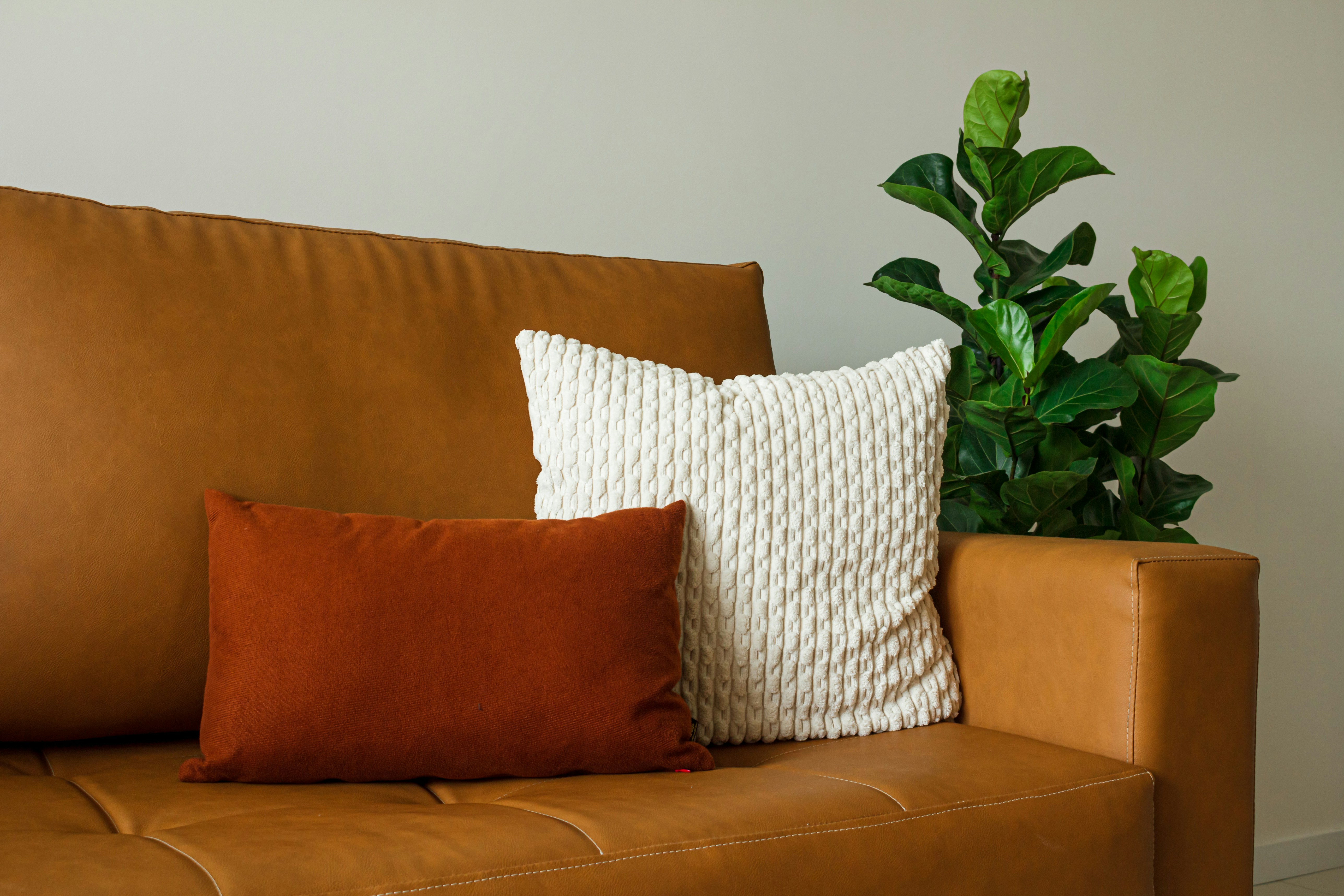 Woman arranging pillows on sofa in living room - Stylish, well-lit living room with cozy borro decor and a caramel synthetic sofa. Modern comfort and ambiance.